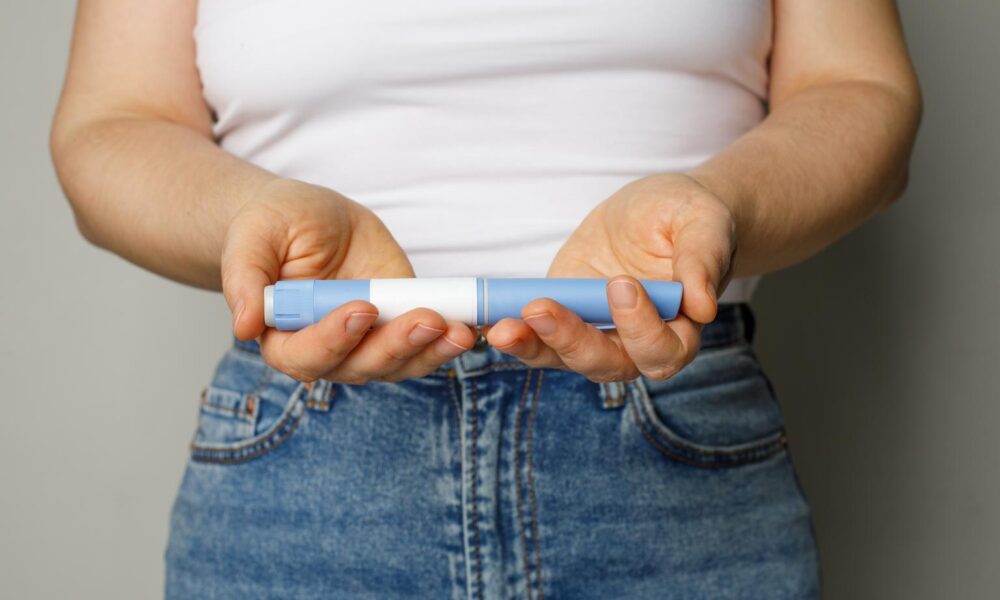 Blue Injection pen in female hand closeup. Semaglutide or insulin drug against female belly. Diabetes and Weight Loss concept.
